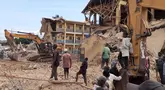 Petugas penyelamat menggunakan alat berat di lokasi sekolah yang sebelumnya runtuh, sementara warga berkumpul untuk mengamati upaya penyelamatan di distrik Jos North di Negara Bagian Plateau, Nigeria, Jumat (12/7/2024). (Muhammad Tanko Shittu / AFP)