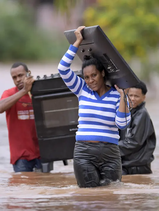 Orang-orang mengarungi air saat mereka memindahkan barang-barang dari rumah mereka yang terendam banjir di negara bagian Minas Gerais di kotamadya Juatuba, Brasil (10/1/2022). Hujan deras yang turun dalam beberapa hari terakhir di bagian tenggara negara itu membuat banjir besar. (AFP/Douglas Magno)