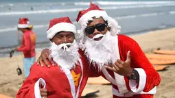 Dua orang pria berpose dengan mengenakan kostum Santa Claus di Pantai Kuta, Bali, Senin (10/12). Setiap tahunnya, ribuan wisatawan mendatangi Bali saat menjelang natal dan tahun baru. (AFP PHOTO / Sonny Tumbelaka)