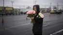 Seorang pria menunggu bus dengan buket bunga segar dari pasar bunga pada Hari Perempuan Internasional di Moskow, Rusia, 8 Maret 2022. (AP Photo)