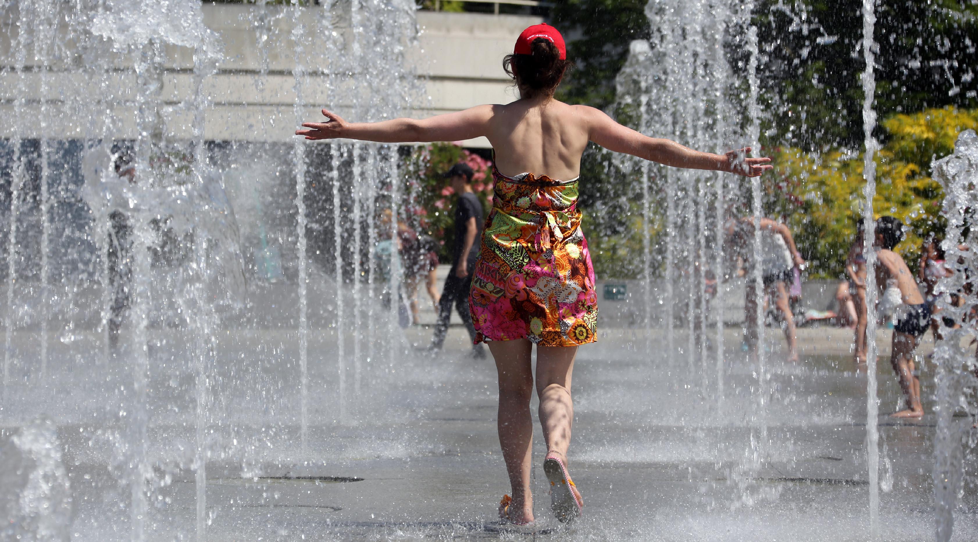Seorang wanita menyegarkan dirinya di air mancur taman Andre Citroen, Paris, Senin (19/6). Suhu temperatur di ibu kota Prancis ini mencapai 36 derajat celcius. (AFP Photo / LUDOVIC MARIN)