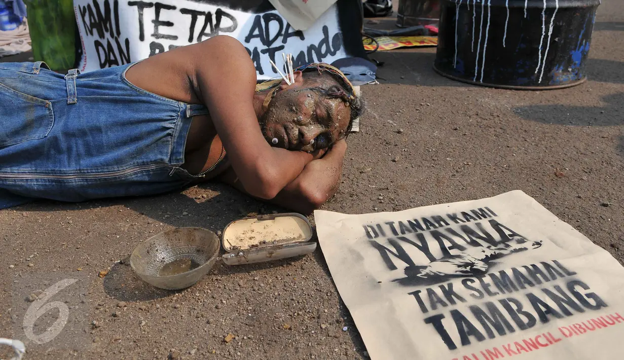 Pengunjuk rasa dengan menyiram tubuhnya dengan pasir saat aksi teaterikal di depan Istana Negara, Jakarta, Kamis (1/10). Mereka meminta kepolisian mengusut tuntas kasus Salim Kancil yang dianiaya dan dikeroyok hingga tewas. (Liputan6.com/Gempur M Surya)