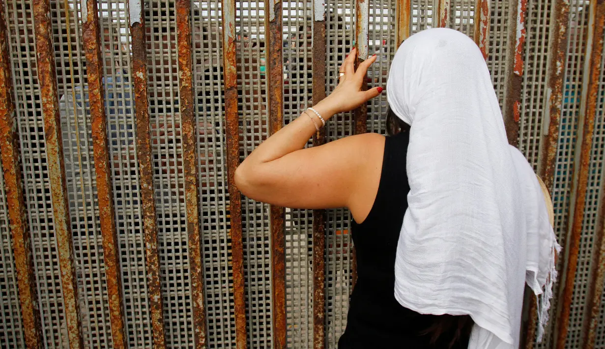 Seorang wanita berbincang dengan keluarga mereka di pagar perbatasan antara Meksiko dan Amerika Serikat, Tijuana, Meksiko (19/11). Pagar pembatasan ini memisahkan antara Meksiko dan Amerika Serikat. (Reuters/Jorge Duenes)