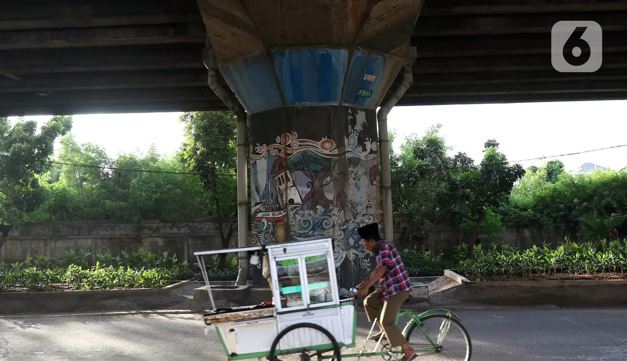 Pedagang melintasi sisi tiang penyangga Jalan Tol Pelabuhan Lingkar Dalam Jakarta di Jalan Ancol Timur, Jakarta, Selasa (16/6/2020). Seni mural yang dulu menghiasi tiang-tiang jalan tol di kawasan tersebut kini terlihat kusam dan berdebu. (Liputan6.com/Helmi Fithriansyah)