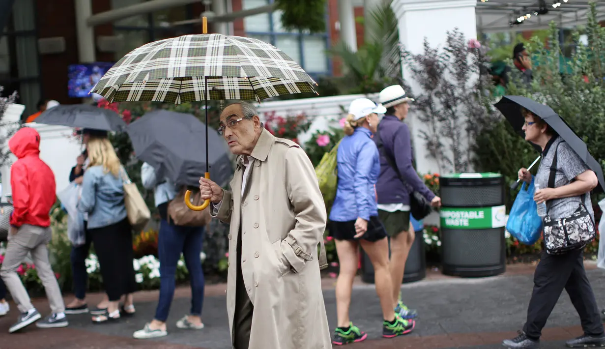Don Kregsman (tengah) berjalan saat hujan turun di lapangan Pusat Tenis Nasional Billie Jean King, New York (29/8). Meski hujan, para penonton tetap antusias menunggu pertandingan tenis tersebut. (AP Photo / Michael Noble)