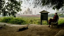 Biksu Buddha duduk di seberang Taj Mahal dari tepi sungai Yamuna di Agra, Jumat (4/5). Sejumlah pihak mengatakan perubahan warna Taj Mahal kemungkinan besar disebabkan pembangunan konstruksi di sekitarnya dan kotoran serangga. (AFP/CHANDAN KHANNA)