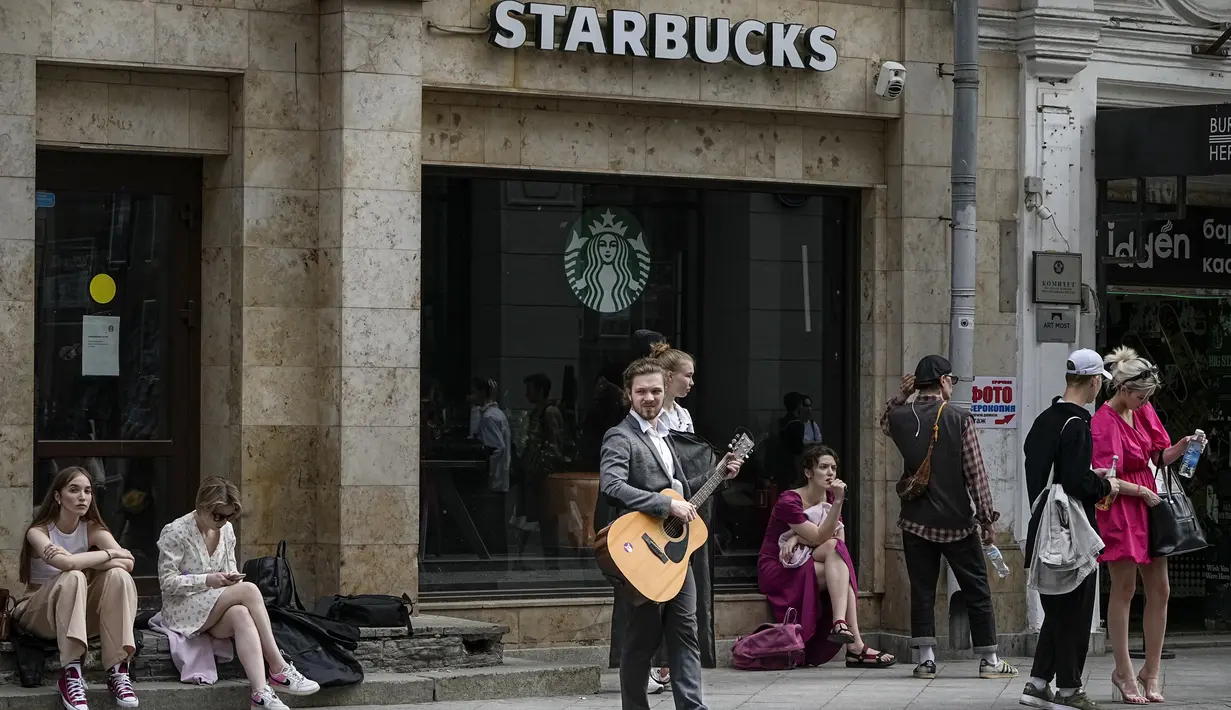 Seorang pemuda bermain gitar di depan kafe jalanan Starbucks yang ditutup akibat sanksi, di Moskow, Rusia, Kamis, 2 Juni 2022. Ketika invasi Rusia ke Ukraina memasuki hari ke-100, kehidupan di Moskow dan St. Petersburg sebagian besar tetap normal, bahkan ketika banyak pengecer Barat mulai hengkang dari negara itu. (AP Photo/Alexander Zemlianichenko)