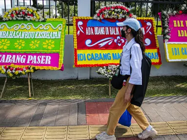 Seorang wanita melintas di depan karangan bunga yang memenuhi luar gedung DPR MPR RI, Jalan Gatot Subroto, Jakarta Pusat, Rabu(12/4/2023). (Liputan6.com/Faizal Fanani)