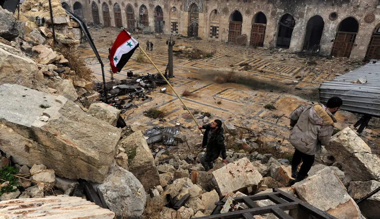 Anggota pasukan Presiden Suriah Bashar al-Assad, mengibarkan bendera Suriah di antara puing bangunan yang hancur karena gempuran senjata selama perang saudara berlangsung, di kompleks Masjid Umayyad, Aleppo, 13 Desember 2016. (REUTERS/Omar Sanadiki)