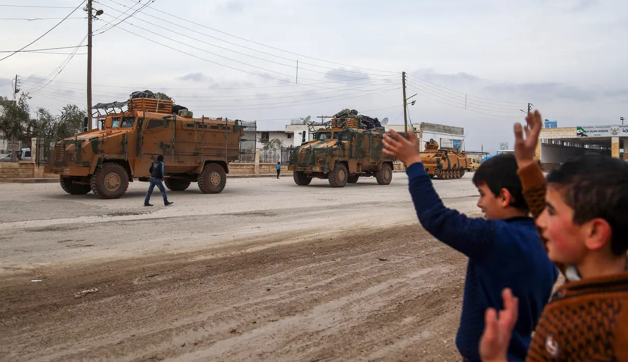 Sejumlah anak-anak melambaikan tangan ke iring-iringan pasukan lapis baja Turki (APC) yang melewati persimpangan perbatasan Bab al-Salamah antara Suriah dan Turki di utara provinsi Aleppo (21/1). (AFP/ Nazeer al-Khatib)