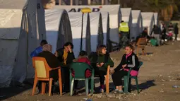 Orang-orang yang kehilangan rumah akibat gempa dahsyat, duduk di luar tenda mereka di kamp darurat, di kota Iskenderun, Turki selatan, Selasa, 14 Februari 2023. Mereka berada di tenda-tenda yang penuh sesak atau berbaris di jalan-jalan untuk menikmati makanan hangat saat pencarian korban selamat yang putus asa memasuki jam-jam terakhir. (AP Photo/Hussein Malla)