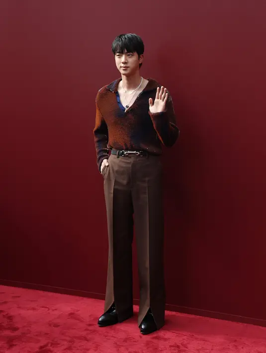 Jin BTS mengenakan sweater rajutan warna-warni yang memantulkan warna dari merah marun hingga oranye dan ungu. Celana cokelat yang disesuaikan melengkapi penampilannya, yang dilengkapi dengan ikat pinggang Horsebit hitam dan sepatu loafer Horsebit klasik merek tersebut, juga berwarna hitam.   [Dok/Gucci].