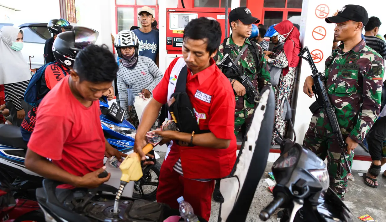 Tentara berjaga saat korban gempa dan tsunami mengantre untuk mendapatkan bahan bakar minyak (BBM) di SPBU Kota Palu, Sulawesi Tengah, Senin (1/10). Pengawalan oleh tentara bersenjata untuk menghindari penjarahan oleh warga. (Jewel Samad/AFP)