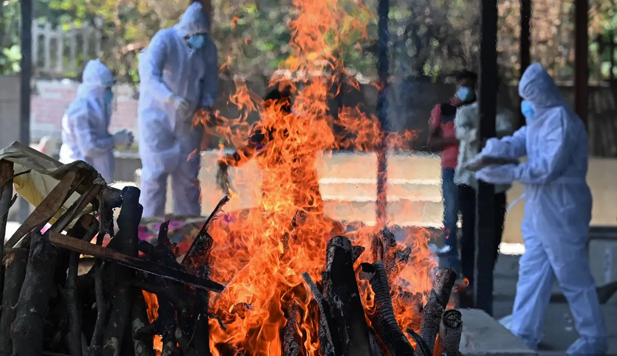 Anggota keluarga dan kerabat yang mengenakan alat pelindung diri menyiapkan tumpukan kayu pemakaman untuk mengkremasi korban COVID-19 di krematorium di New Delhi, India, Senin (24/5/2021). Kematian akibat COVID-19 di India telah menembus 300 ribu orang. (Sajjad HUSSAIN/AFP)