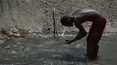 Seorang pria mengeluarkan lumpur dari dasar saluran pembuangan saat dia mencari logam berharga di Sungai Guaire, di Caracas, Venezuela (1/2). Puluhan warga mencari logam atau tembaga setiap hari di Sungai Guaire. (AFP Photo/Federico Parra)