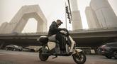 Seorang pria yang mengenakan masker mengendarai skuter di sepanjang jalan di kawasan pusat bisnis di Beijing, Rabu, 22 Maret 2023. (AP Photo/Mark Schiefelbein)