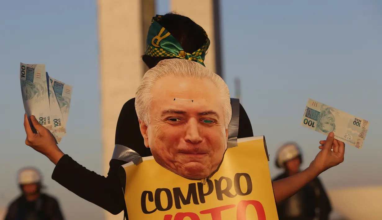 Seorang wanita memegang uang palsu dan poster bergambar Presiden Brasil Michel Temer pada unjuk rasa di depan Kongres Nasional, Brasilia, Rabu (2/8). Para demonstran membanjiri jalanan kota sejak Rabu waktu setempat. (AP/Eraldo Peres)