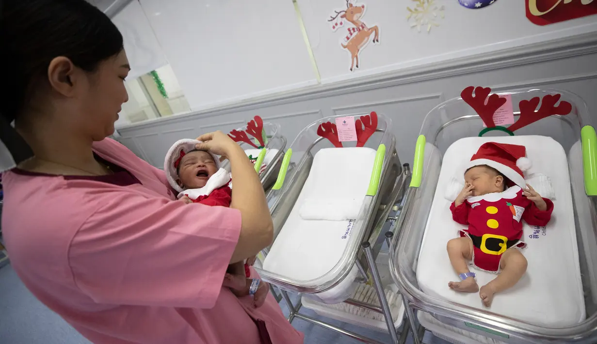Perawat menggendong bayi yang baru lahir di Rumah Sakit Synphaet, Bangkok, Thailand, Selasa (24/12/2019). Bayi-bayi tersebut dipakaikan kostum sinterklas untuk menyambut Hari Raya Natal. (AP Photo/Sakchai Lalit)