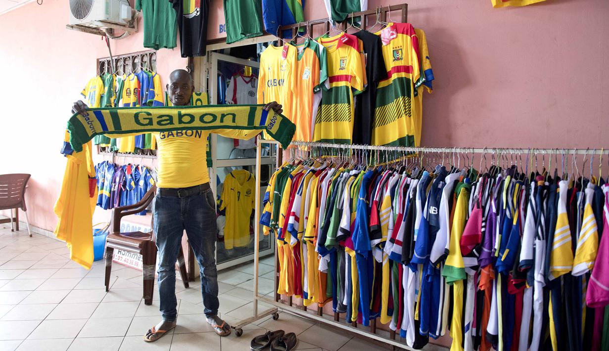 Seorang pedagang membentangkan Merchandise bertuliskan Gabon di Port-Gentil (18/1/2017). Pada Piala Afrika 2017 ini Gabon tergabung di Grup A bersama Kamerun, Burkina Faso , Guinea-Bissau.  (AFP/Justin Tallis)