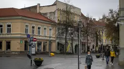 Penduduk lokal berjalan di Kota Tua yang kosong di Vilnius, Lithuania (7/11/2020). Seluruh wilayah telah dikunci selama tiga minggu secara nasional dari 7 November hingga 29 November, yang memberlakukan pembatasan pada kehidupan sosial dan kegiatan ekonomi.  (AP Photo/Mindaugas Kulbis)
