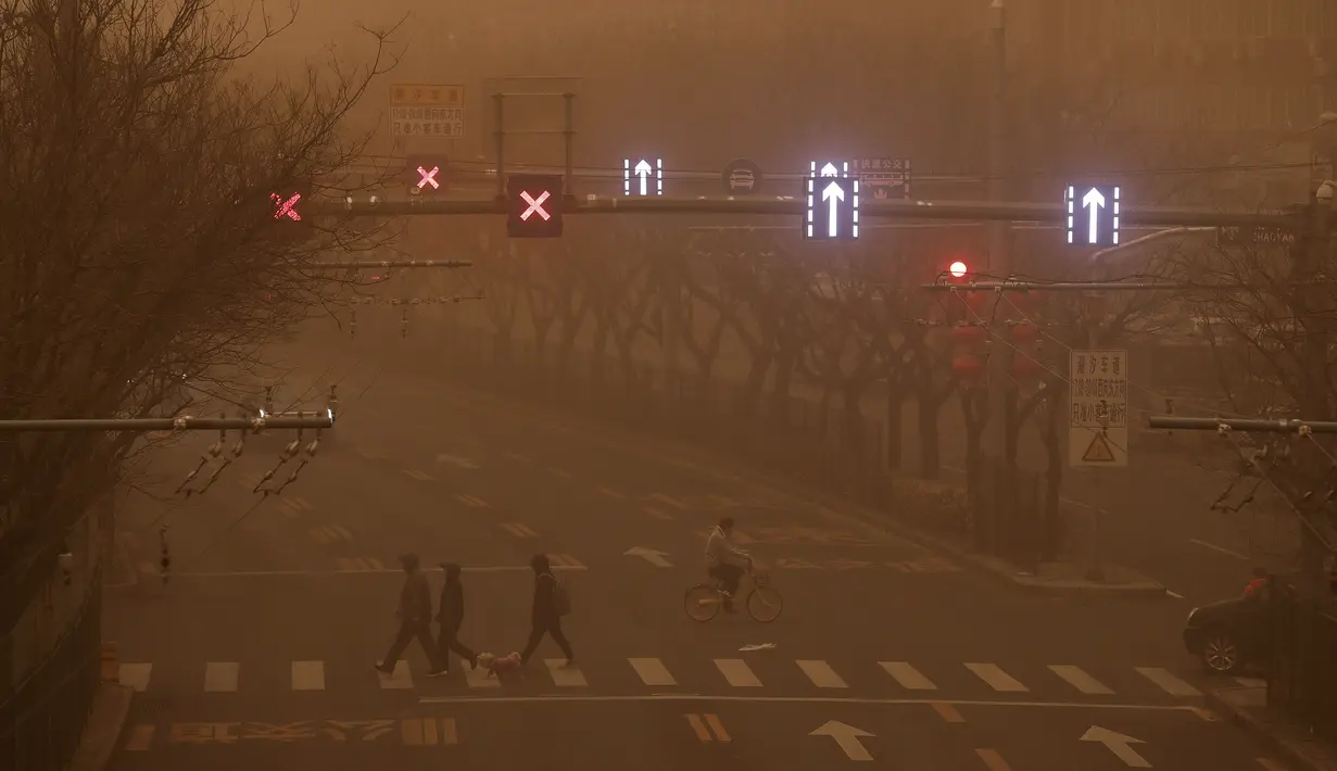Orang-orang berjalan di seberang jalan saat ibu kota dilanda polusi udara dan badai pasir di Beijing, Senin (15/3/2021). (AP Photo/Andy Wong)
