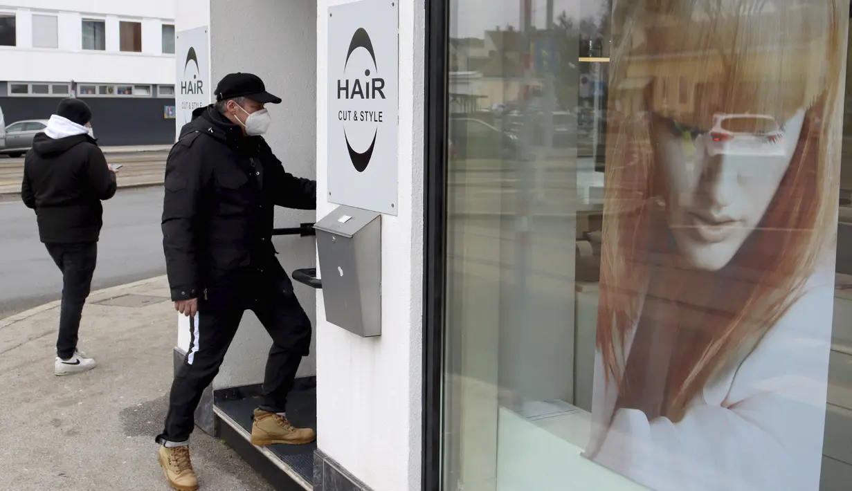 Seorang pria bermasker pergi ke penata rambut yang dibuka kembali setelah pelonggaran lockdown di Wina, Austria, Senin (8/2/2021). Austria mulai melonggarkan lockdown covid-19 ketiga mereka mulai 8 Februari dengan mengizinkan sekolah, museum dan toko dibuka kembali. (AP Photo/Ronald Zak)