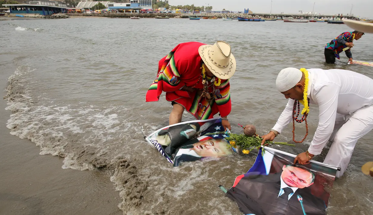 Dukun Peru mencuci poster Presiden Terpilih AS Donald Trump dan Presiden Rusia, Vladimir Putrin saat menggelar ritual di Pantai Agua Dulce di Lima, Peru, (29/12). Dukun tersebut juga meramalkan banyaknya serangan teroris di Eropa. (Reuters/Mariana Bazo)