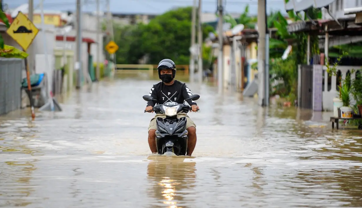 Seorang pria mengendarai sepeda motornya menerjang banjir di Batu Berendam, Malaka, Malaysia, 3 Januari 2022. Banjir besar masih terus menerjang negeri jiran Malaysia. (NAZRULHAD HASHIM/AFP)