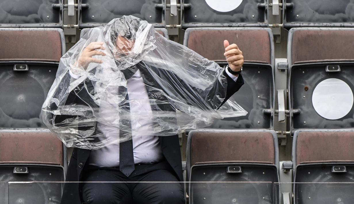 Menteri Olahraga Italia, Vincenzo Spadafora, berusaha menggunakan jas hujan saat pertandingan final Italia Terbuka Putra antara Novak Djokovic melawan Diego Schwartzman di Foro Italico, Roma, pada 21 September 2020. (AFP/Riccardo Antimiani/pool)