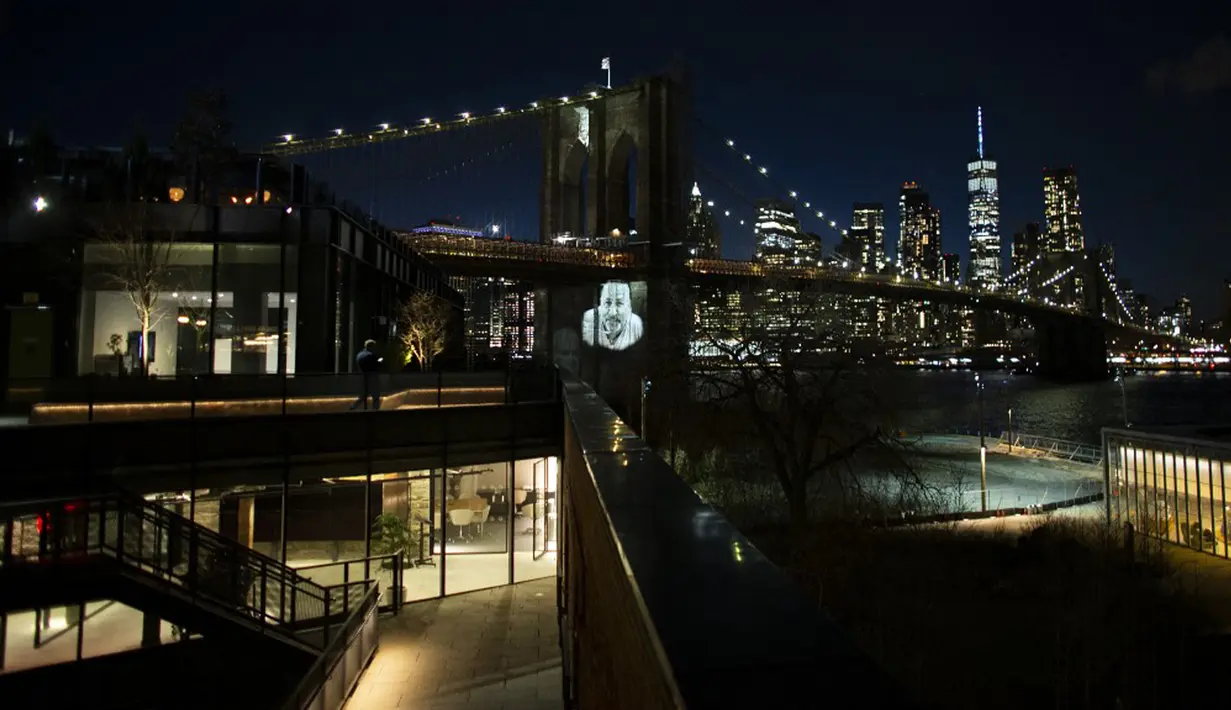 Gambar korban diproyeksikan pada Jembatan Brooklyn saat Hari Peringatan COVID-19 di Brooklyn, New York, Amerika Serikat, 14 Maret 2021. Acara penghormatan yang digelar kepada 30.258 kematian di New York, terjadi setelah satu tahun berlalu dimulainya pandemi di AS. (Kena Betancur/AFP)