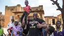 Iron Biby mengangkat seorang anak di halaman rumah neneknya di Bobo-Dioulasso pada 24 September 2018. Prestasinya ini membuat Biby terkenal di Burkina Faso hingga orang-orang memujanya dan anak-anak selalu mengagumi ototnya. (OLYMPIA DE MAISMONT / AFP)