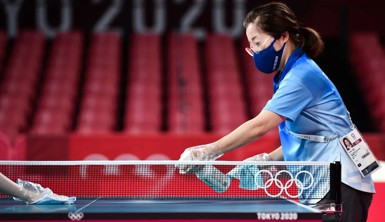 Seorang relawan membersihkan meja selama sesi latihan tenis meja di Tokyo Metropolitan Gymnasium, Tokyo, pada 21 Juli 2021, menjelang Olimpiade Tokyo 2020. (AFP/Jung Yeon-je)