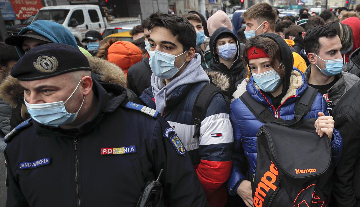 Polisi berdiri di depan remaja yag antre di luar restoran untuk mendapatkan burger gratis yang ditawarkan selama promosi di Bucharest, Rumania, Senin (1/2/2021). Ratusan orang berkerumun demi burger gratis hingga polisi mendenda restoran karena tidak mematuhi protokol COVID-19. (AP/Vadim Ghirda)
