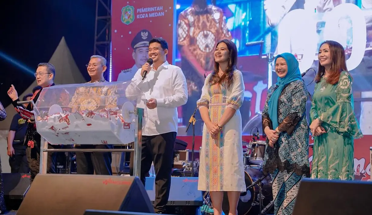 Ayu elegan Kahiyang tampil di atas panggung bersama sang suami mengenakan dress midi berwarna dasar putih dengan corak wastra. [Foto: Instagram/bobbynst]