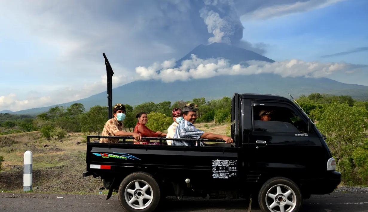 Sejumlah warga mengenakan masker menaiki mobil bak terbuka saat melewati Gunung Agung di Kabupaten Karangasem, Bali (27/11). (AFP/Sonny Tumbelaka)
