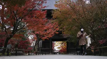 Seorang perempuan yang mengenakan masker mengunjungi kuil Buddha Joshinji saat pengunjung mengamati warna dedaunan musim gugur di Tokyo, Jepang pada 9 Desember 2020. (AP Photo/Kiichiro Sato)