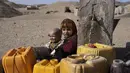 Dua anak Afghanistan duduk di sebelah keran ketika warga desa Kamar Kalagh di luar Herat, mengisi wadah plastik mereka dengan air, pada 26 November 2021. Kekeringan Afghanistan, yang terburuk dalam beberapa dekade, kini memasuki tahun kedua, diperburuk oleh perubahan iklim. (AP/Petros Giannakouris)