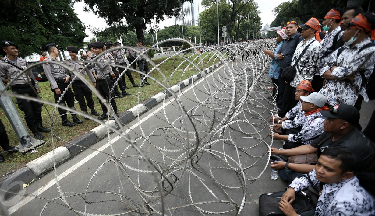 Massa dari Forum Honorer Kategori 2 (FHK2I) dan aparat kepolisian berdiri berhadapan di batasi barikade kawat berduri yang dipasang di seputaran Istana Kepresidenan, Jakarta, saat menggelar unjuk rasa, Rabu (10/2). (Liputan6.com/Faizal Fanani)