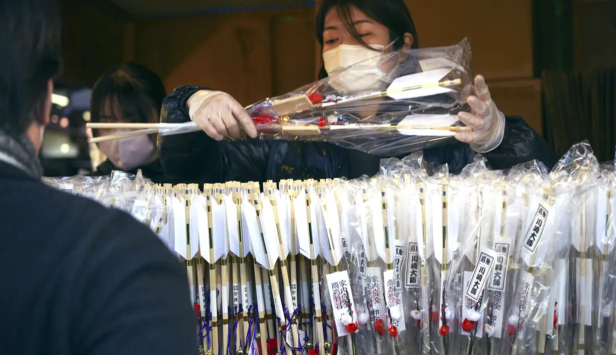 Seorang staf menjual Hamaya, atau panah ritual, untuk mengusir roh jahat di kuil Kawasaki Daishi, di mana banyak pengunjung berdoa untuk keberuntungan selama "hatsumode" atau kunjungan pertama tahun ini ke kuil atau kuil, di Kawasaki, dekat Tokyo , Senin, 2 Januari 2023. (AP Photo/Eugene Hoshiko)