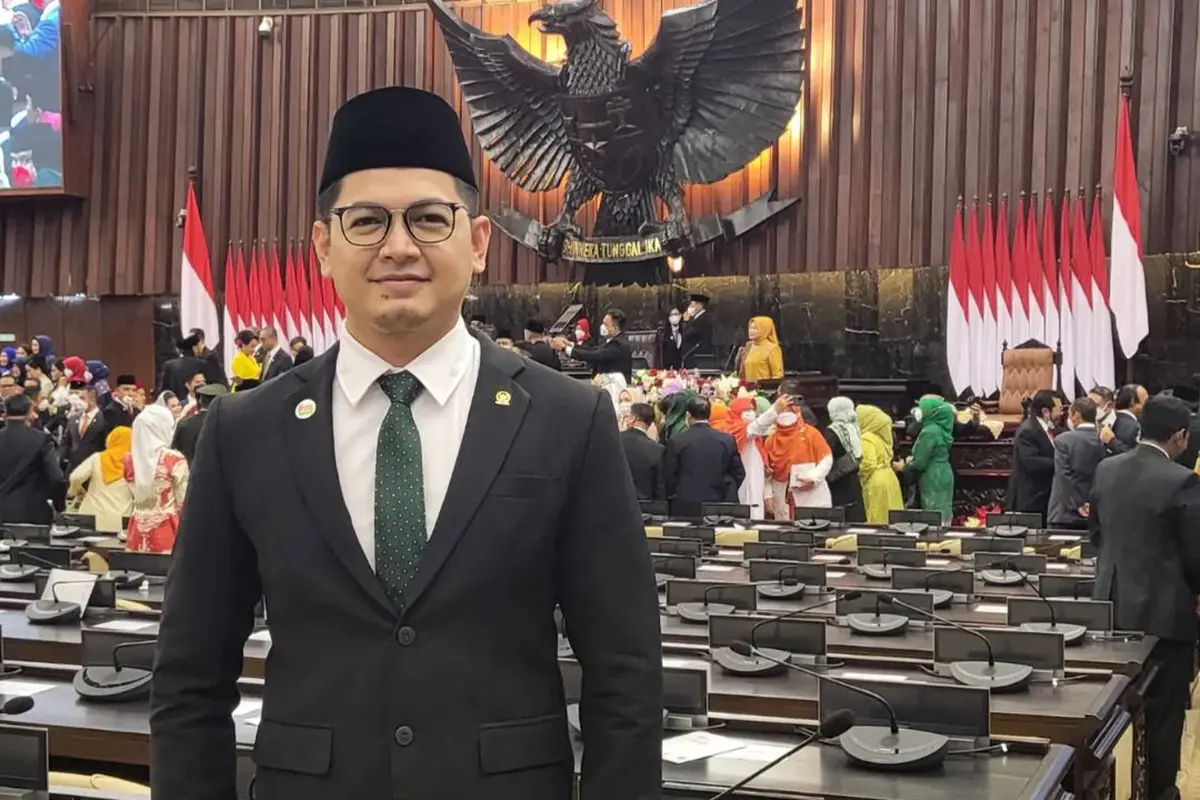 Tommy Kurniawan tampil gagah dengan jas hitam dipadukan dengan kemeja putih serta dasi hijau. Lengkap dengan peci hitamnya, ia berfoto dengan latar belakang meja sidang. (Foto: Instagram/@tommykurniawan)