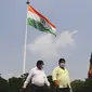 Sejumlah pria mengenakan masker berjalan melewati bendera nasional India di New Delhi (16/9/2020). Total kasus Covid-19 di India melampaui lima juta pada 16 September, data kementerian kesehatan menunjukkan Pandemi meluas cengkeramannya di negara tersebut. (AFP/Sajjad Hussan)