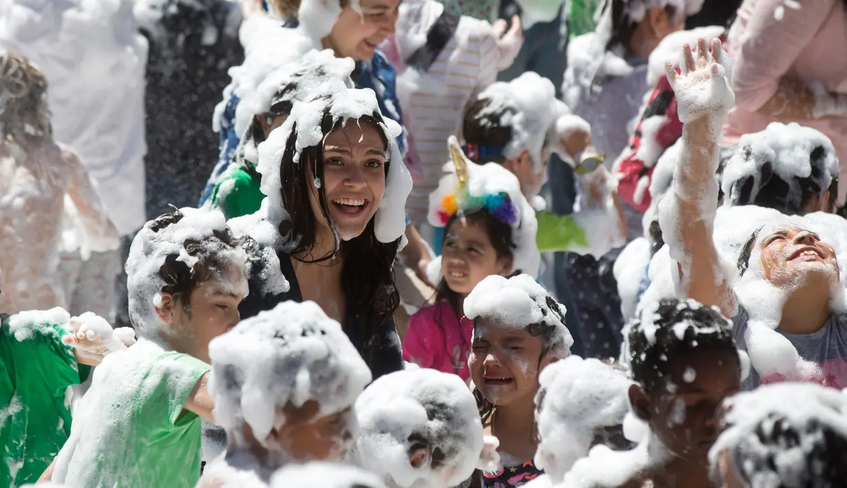 Orang tua dan anak-anak disemprot dengan busa oleh petugas pemadam kebakaran selama pesta di distrik Malasana Madrid, Spanyol, (4/5/2019). (AP Photo/Paul White)