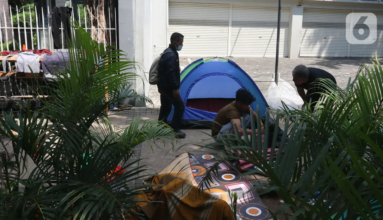 Pejalan kaki melintasi pencari suaka yang tinggal sementara di trotoar kantor UNHCR, Jalan Kebon Sirih, Jakarta, Sabtu (1/5/2021). Para pencari suaka itu menuntut Komisi Tinggi PBB untuk Pengungsi (UNHCR) meminta kejelasan atas status dan memperhatikan nasib mereka. (Liputan6.com/Herman Zakharia)