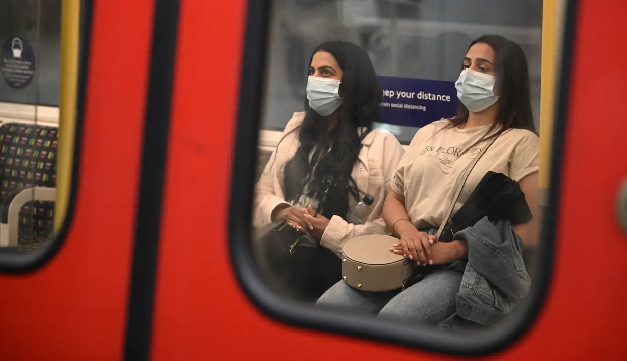 Para penumpang yang mengenakan masker menaiki kereta bawah tanah di pusat kota London, Senin (5/7/2021). PM Inggris Boris Johnson berencana mencabut sebagian besar pembatasan wilayah selama pandemi Covid-19, termasuk penggunaan masker dan jaga jarak mulai 19 Juli. (DANIEL LEAL-OLIVAS/AFP)
