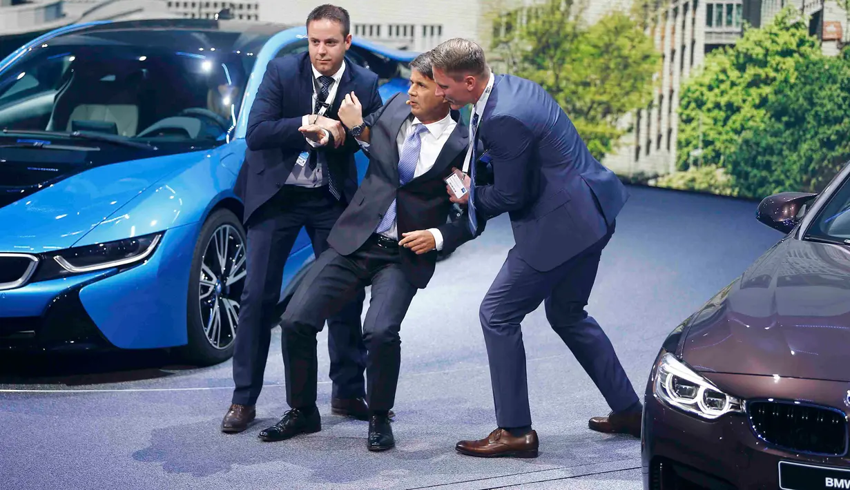 Dua orang tampak membantu CEO BMW, Harald Krueger yang jatuh pingsan saat sedang presentasi selama Frankfurt Motor Show (IAA) di Jerman, Selasa (15/9). Krueger jatuh ketika tengah memberikan ulasan mengenai produk terbaru BMW. (REUTERS/Kai Pfaffenbach)