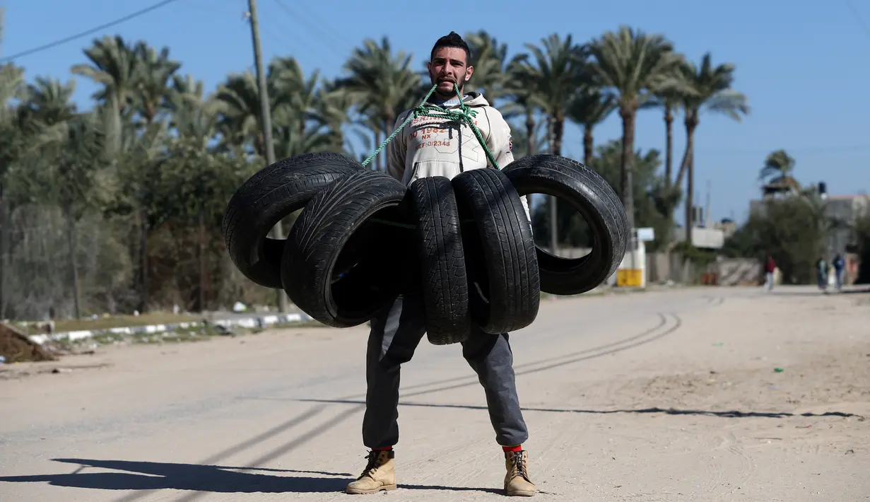 Aksi Mohamed Barka, pria yang dijuluki "Super Hero" asal Palestina saat mengangkat sejumlah ban menggunakan giginya di Deir Al-Balah, Gaza Tengah, Kamis (4/2). (MOHAMMED ABED/AFP)