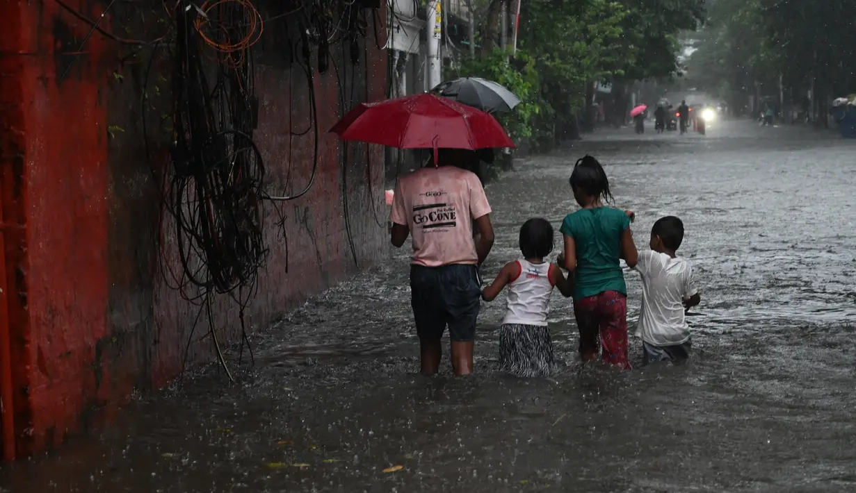 Anak-anak mengarungi jalan yang tergenang air setelah hujan deras di Kolkata (20/9/2021). Hujan dilaporkan dipicu oleh sirkulasi siklon yang terbentuk di atas Teluk Benggala. (AFP/Dibyangshu Sarkar)