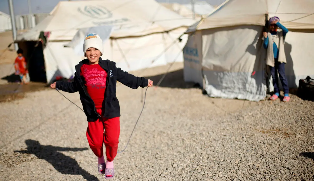 Seorang anak perempuan pengungsi Irak tersenyum saat memainkan tali skipping di Debaga kamp, di pinggiran Erbil, Irak (24/11). (REUTERS/Mohammed Salem) 