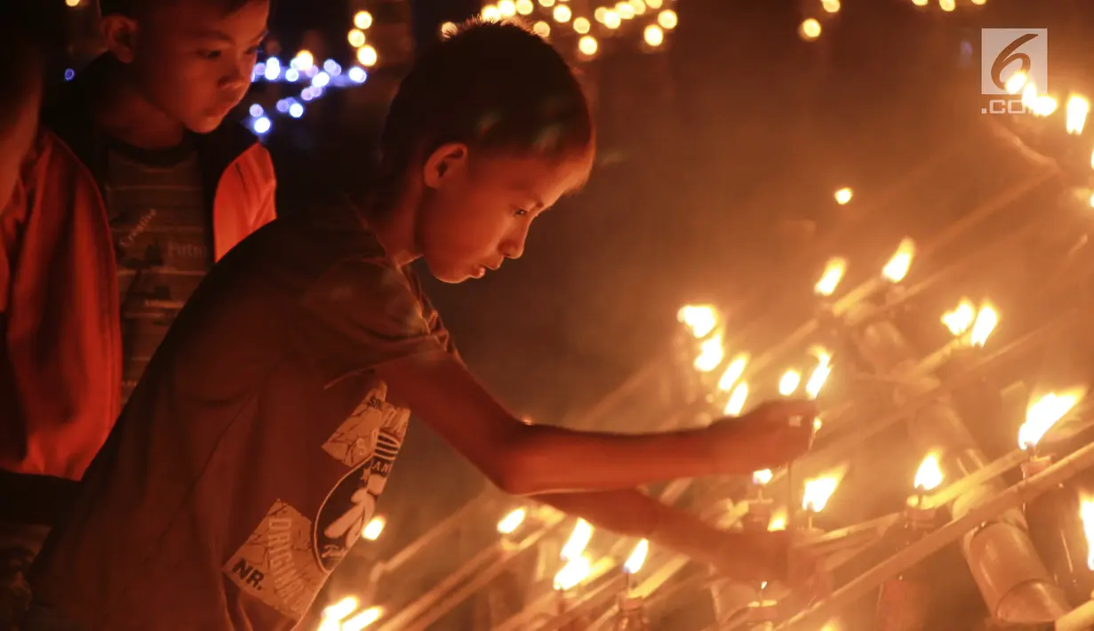Anak-anak menyalakan lampu minyak saat perayaan tumbilotohe atau penyalaan berjuta lampu minyak di akhir Ramadan di Kota Gorontalo, Jumat (31/5/2019). Lampu minyak tersebut dipasang menghiasi jalan, halaman rumah, masjid bahkan sungai. (Liputan6.com/Arfandi Ibrahim)