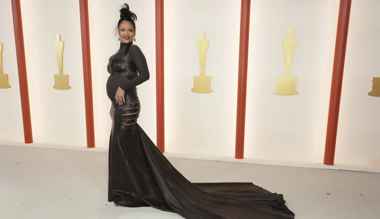 Penyanyi Rihanna berpose untuk fotografer setibanya di karpet sampanye, pengganti karpet merah, Academy Awards ke-95 atau Oscar 2023 di Teater Dolby di Hollywood, California pada Minggu, 12 Maret 2023, waktu setempat. Tampilan itu menunjukkan ekor gaun panjang yang dramatis dan sayatan menyamping di kedua sisi pinggul Rihanna. (Photo by Jordan Strauss/Invision/AP)
